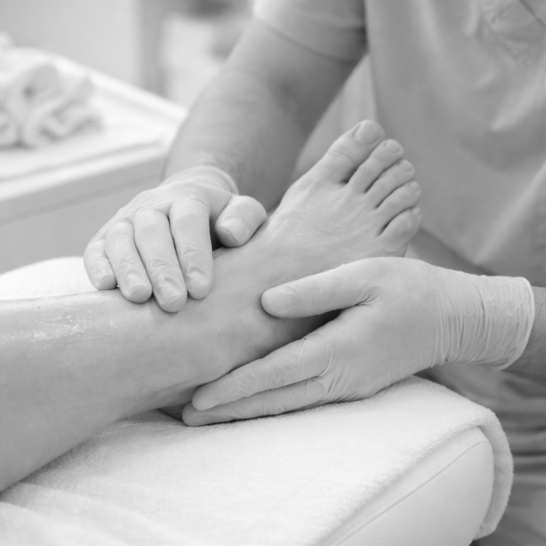 Eine Hand massiert einen Fuß auf einer Liege in einer Behandlungsumgebung.